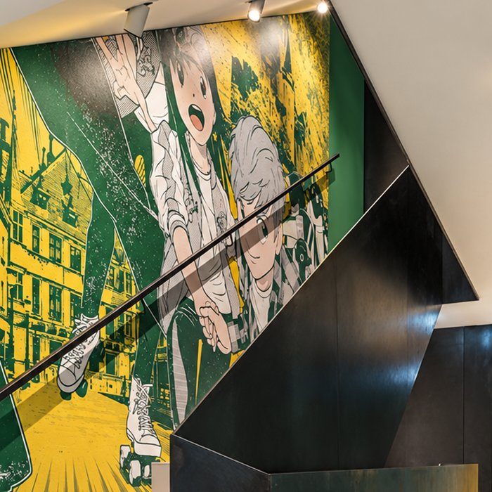 A manga-style mural by Plastered 8 in green and yellow along a stairwell, two skaters racing through Luxembourg's old town