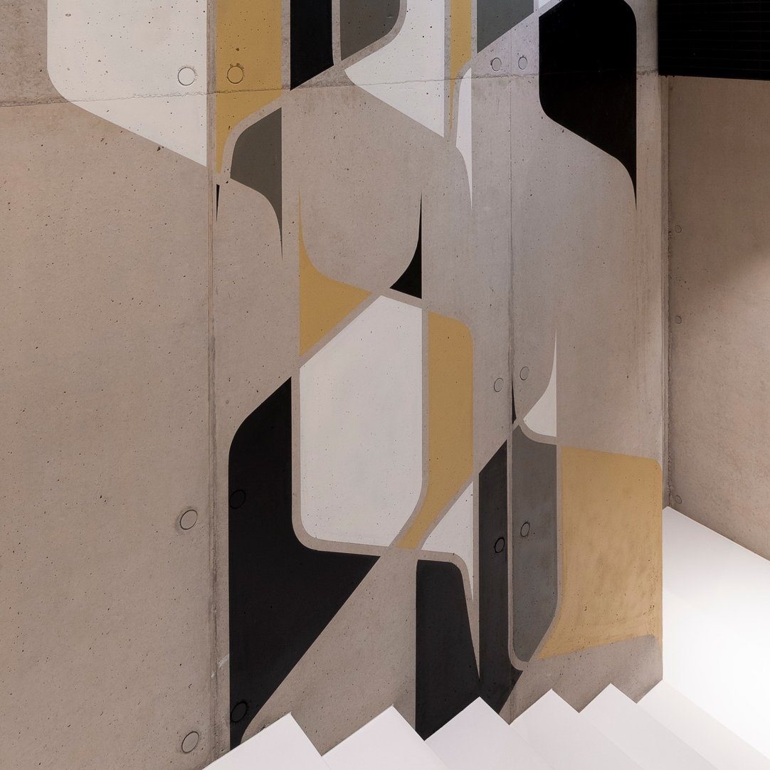 A geometric mural by Spike in black, grey, white and ochre on a concrete stairwell wall