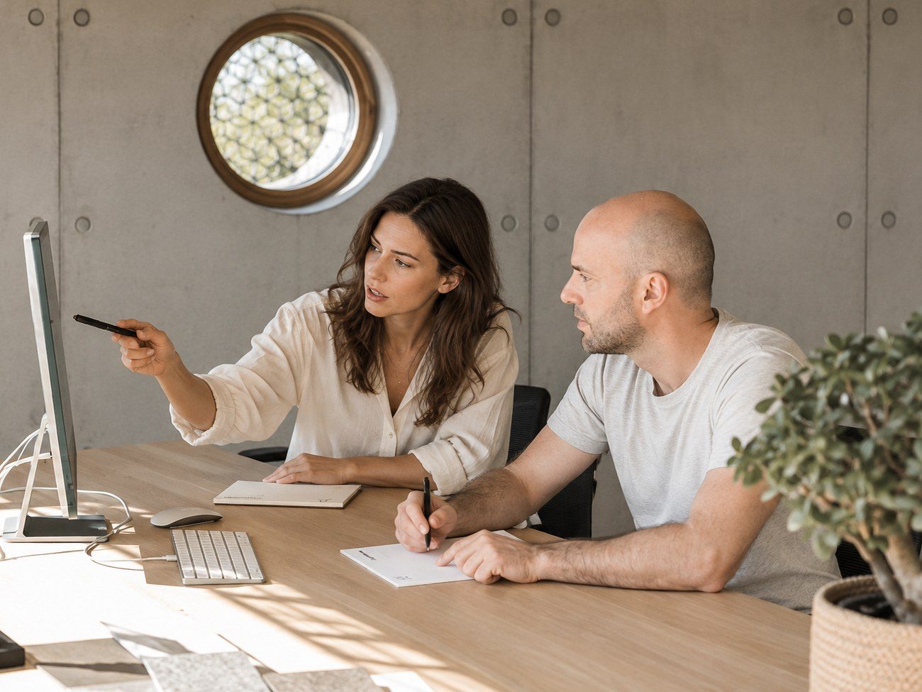 Max Bauer and a founder at a table in a concrete office with a round window: she points at the screen, he takes notes