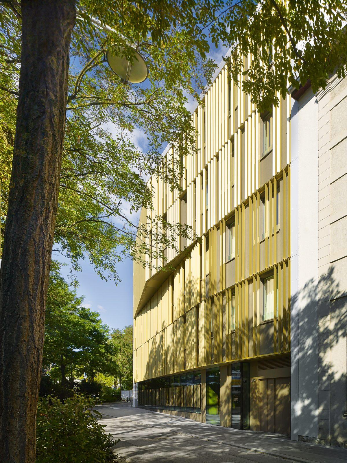 Golden vertical fins on a Polyform building façade, seen through trees