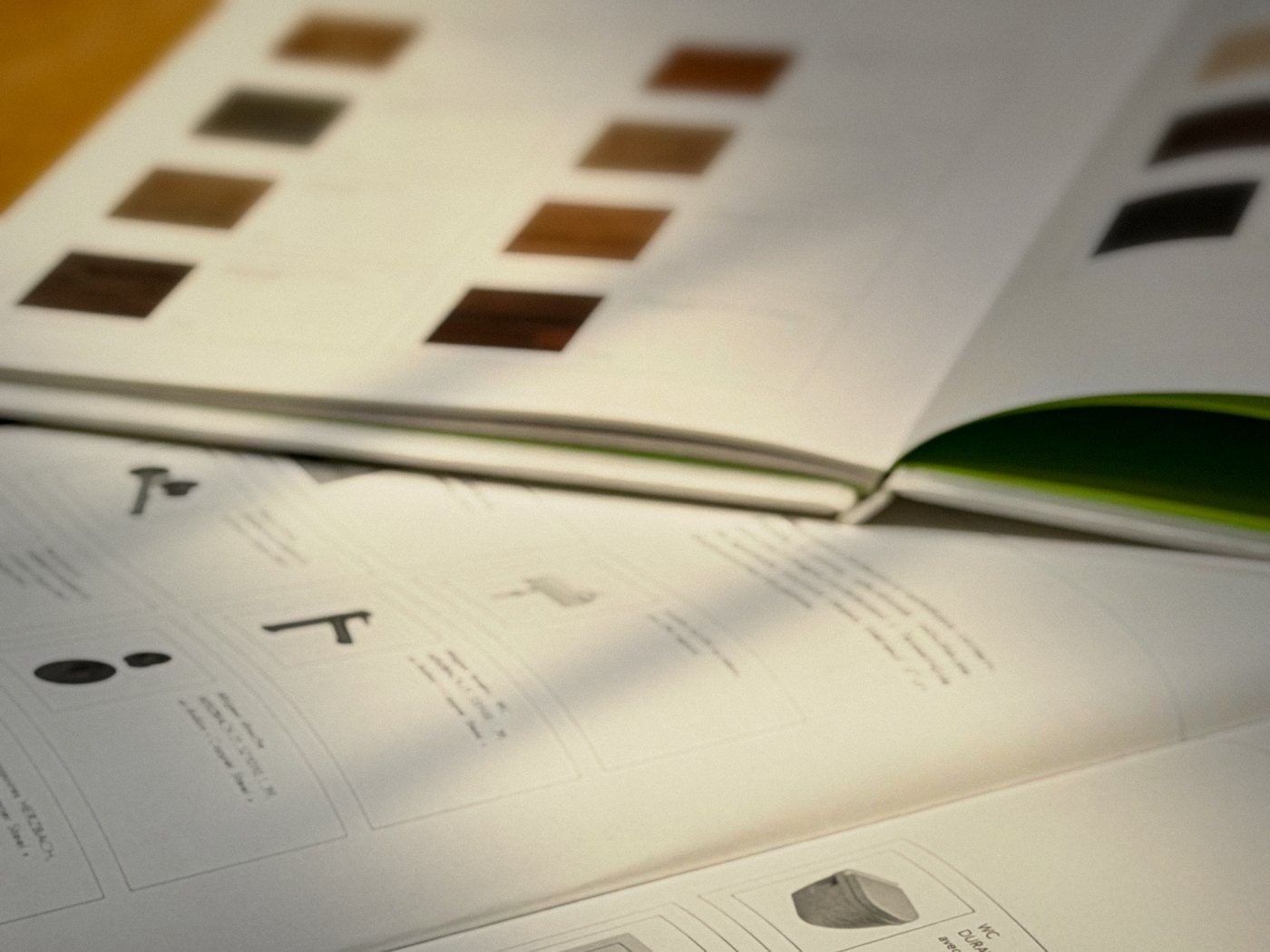 Open buyer catalogues in warm window light: wood samples, fittings and finishes laid out in a fixed grid